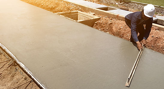 A man in a hard hat is Levelling cement on a sidepath